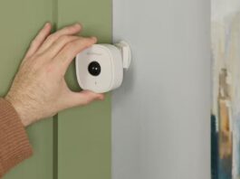 A hand adjusts the Swann wall sensor on a beige wall inside a home.