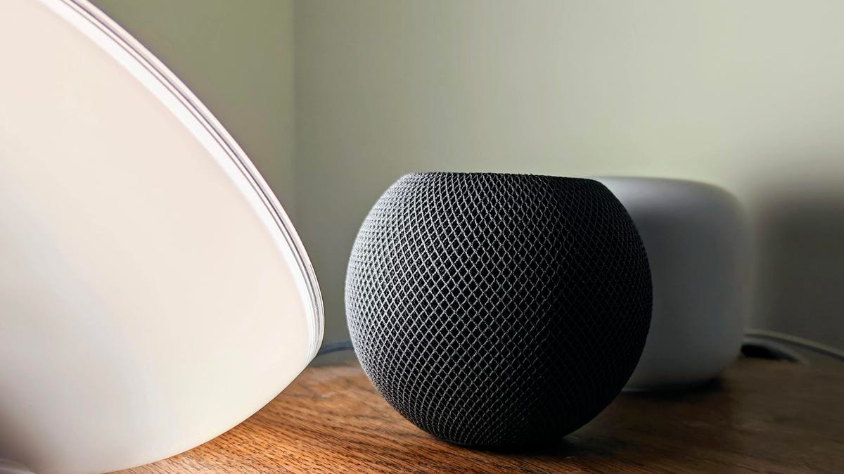 Apple HomePod Mini on a table by Google Nest WiFi router and Philips Hue Go.