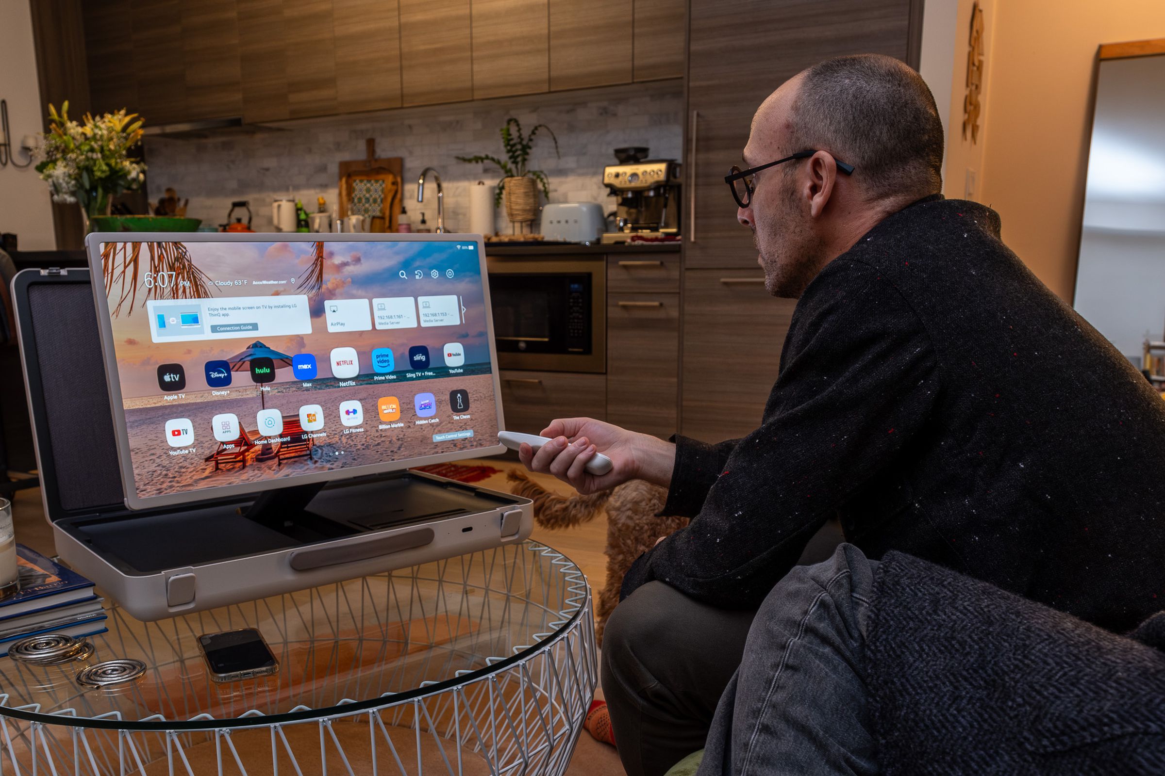 A photo of a man leaning over on a couch and using LG’s StanbyME Go briefcase TV.