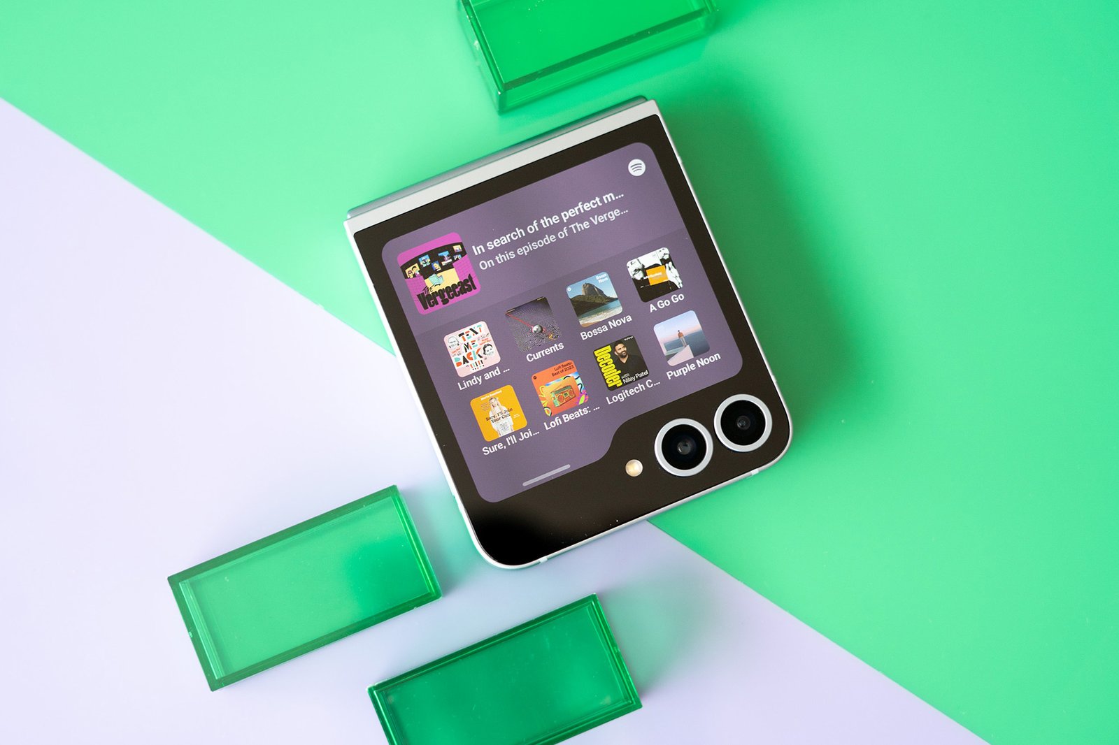 Photo of Samsung Galaxy Z Flip 6 on green and purple background showing cover screen.