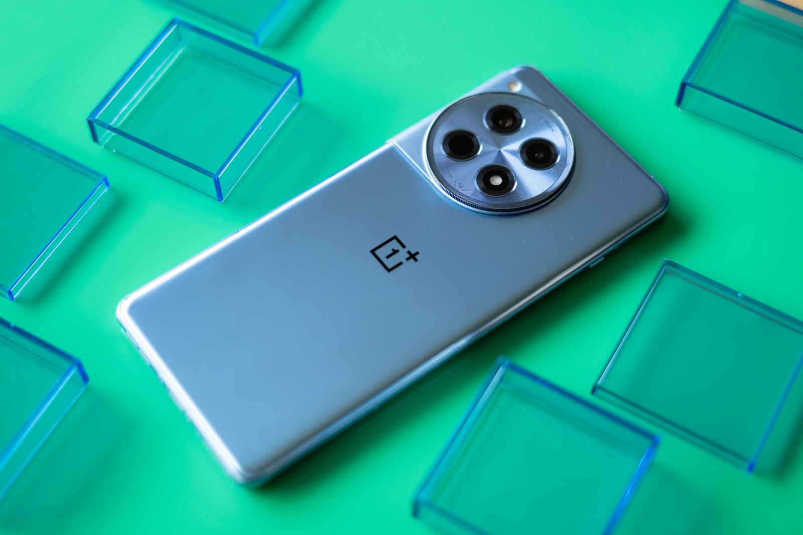 OnePlus 12R on a green background with back panel facing up surrounded by blue translucent squares.