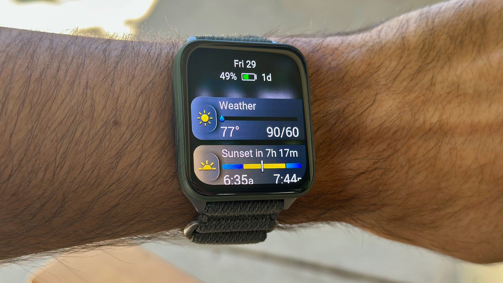The Garmin Venu X1 on the author's wrist, showing the current battery percentage (49%) and time left (1 day) in AOD mode, along with glances for Weather and Sunset below.