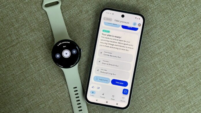 A photo of the Google Pixel Watch 4 sitting next to a Pixel 9a open to the Fitbit app, showing the Fitbit Premium Health Coach preview with the Fitness tab open; it shows a customized workout plan with three upcoming runs.
