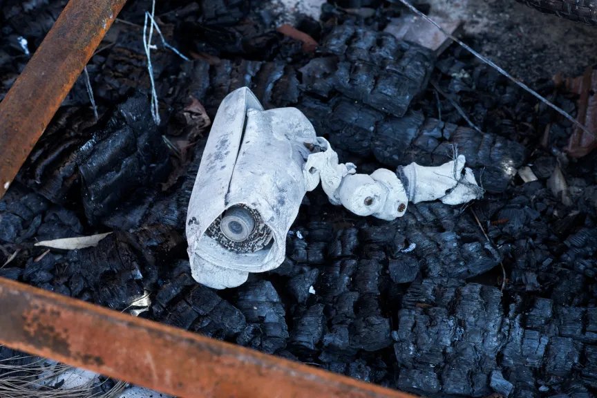 A white burned security camera lying in the ashes.
