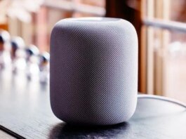 A gray HomePod sits by a window.