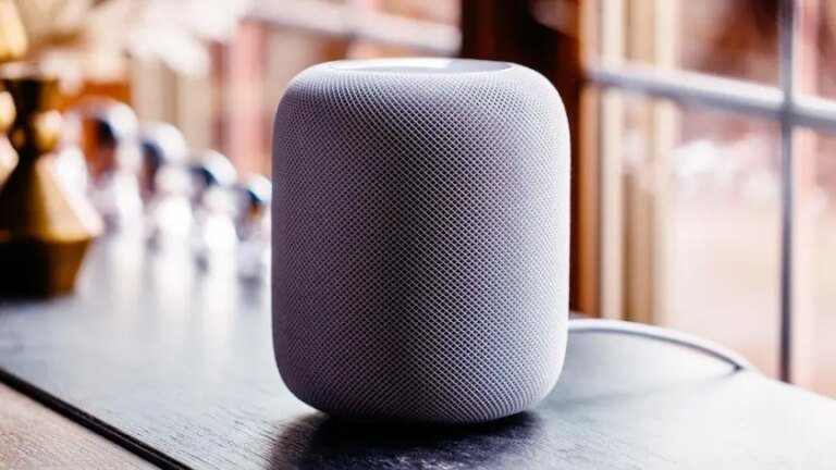 A gray HomePod sits by a window.