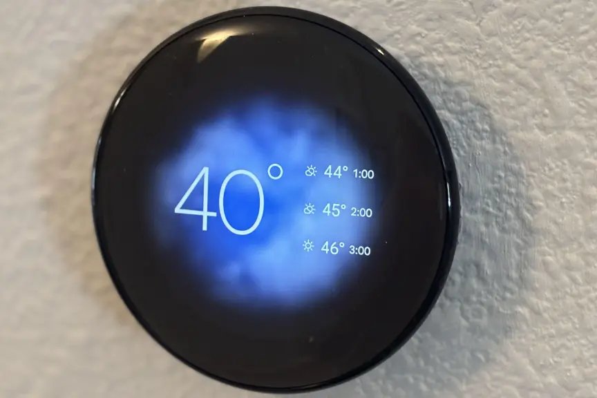 Nest Thermostat on wall showing temps and blue sky graphic.